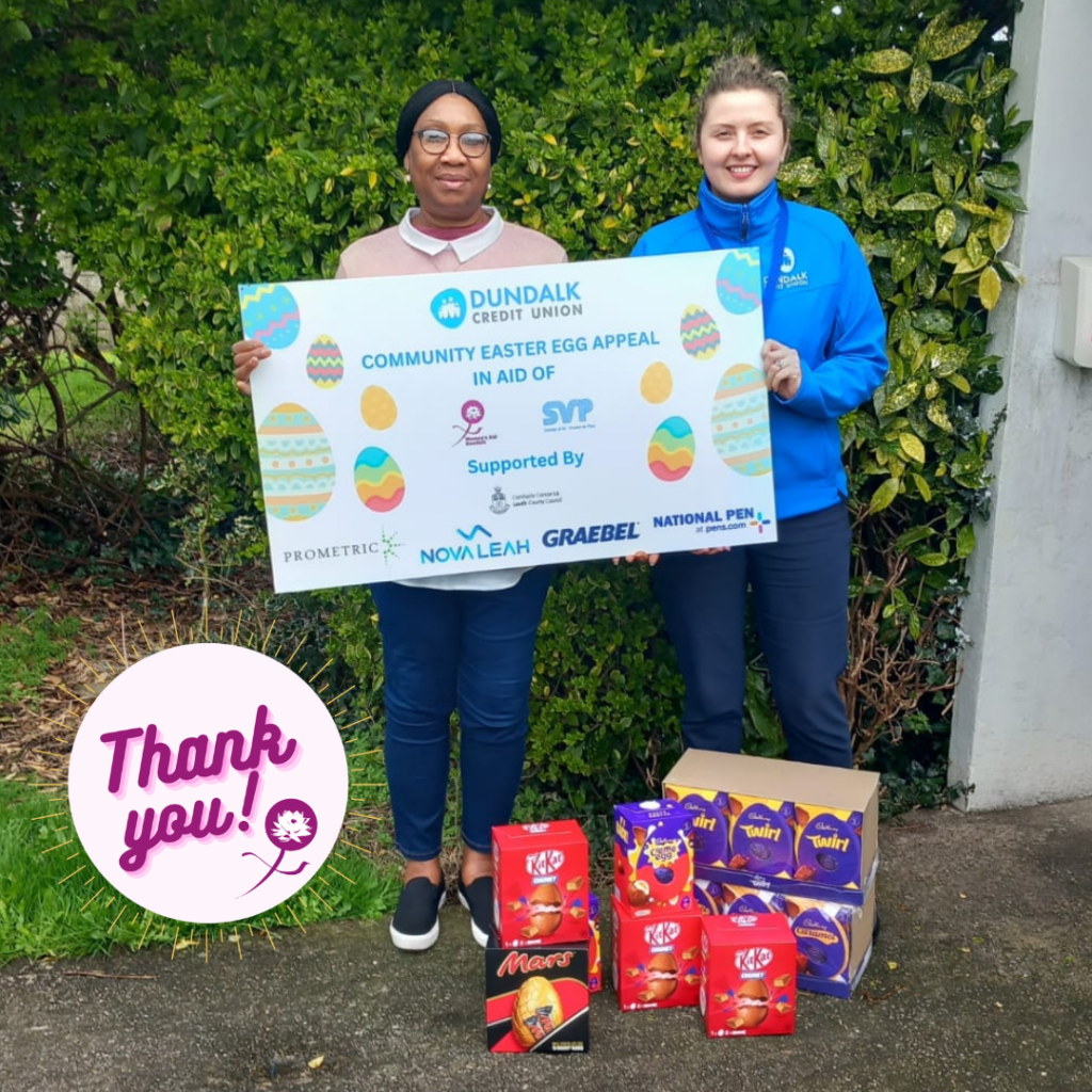 Woman accepting a large cheque from another woman with easter eggs on the ground beside them.